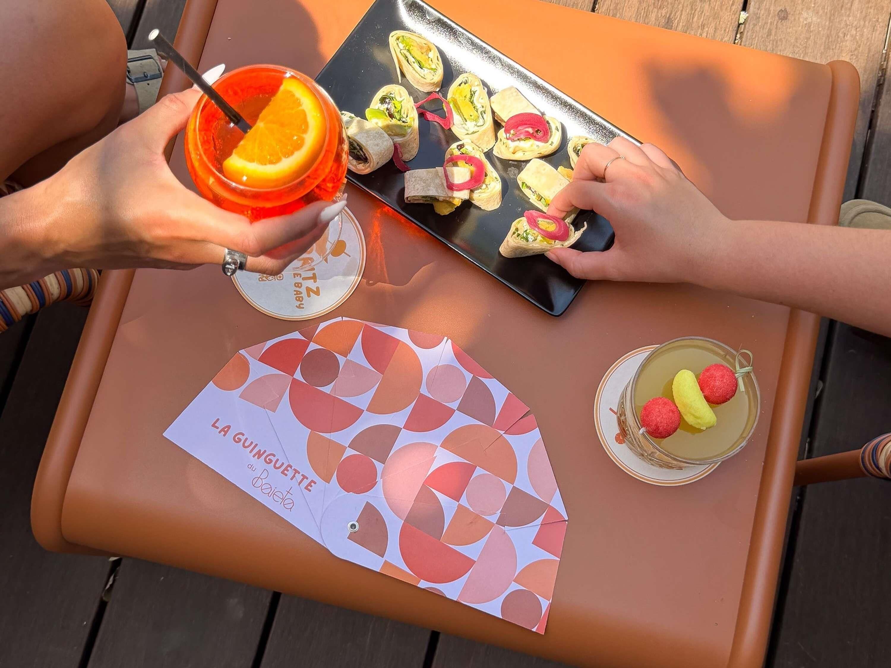 A table with a tray of food, a drink with an orange slice, and a menu.