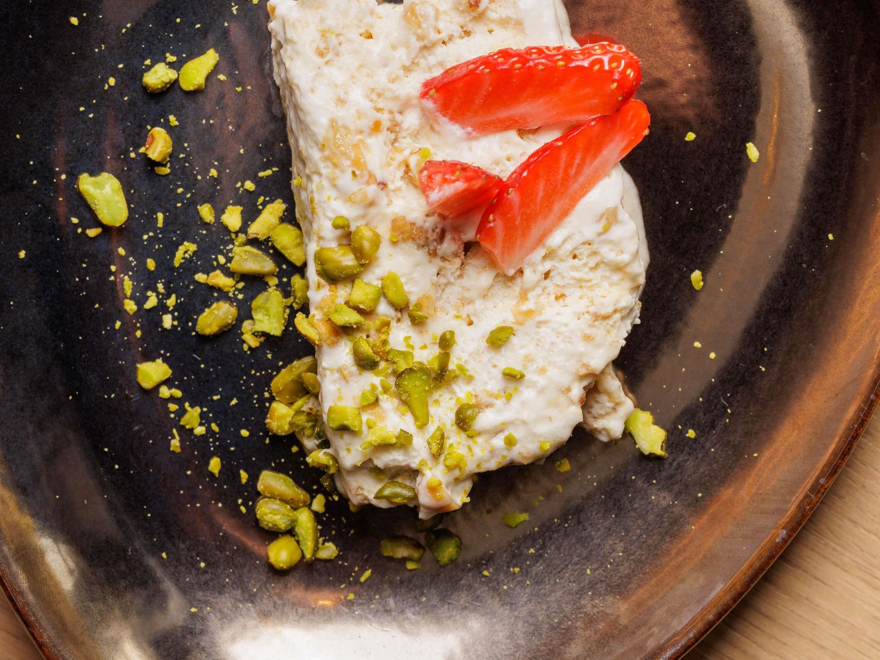 A dessert with whipped cream, strawberries, and chopped pistachios on a dark plate.