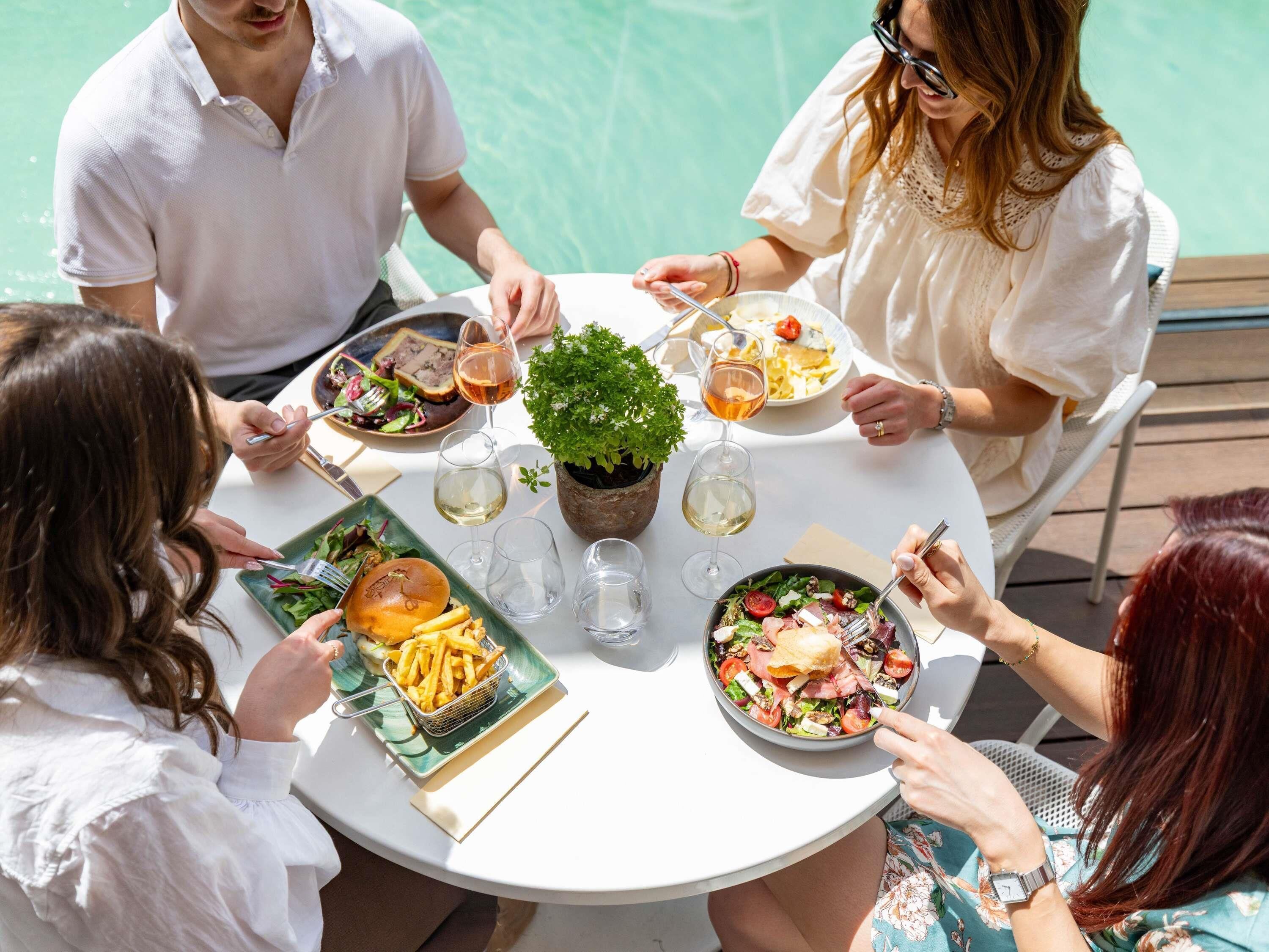 A round table with a potted plant, surrounded by people dining.