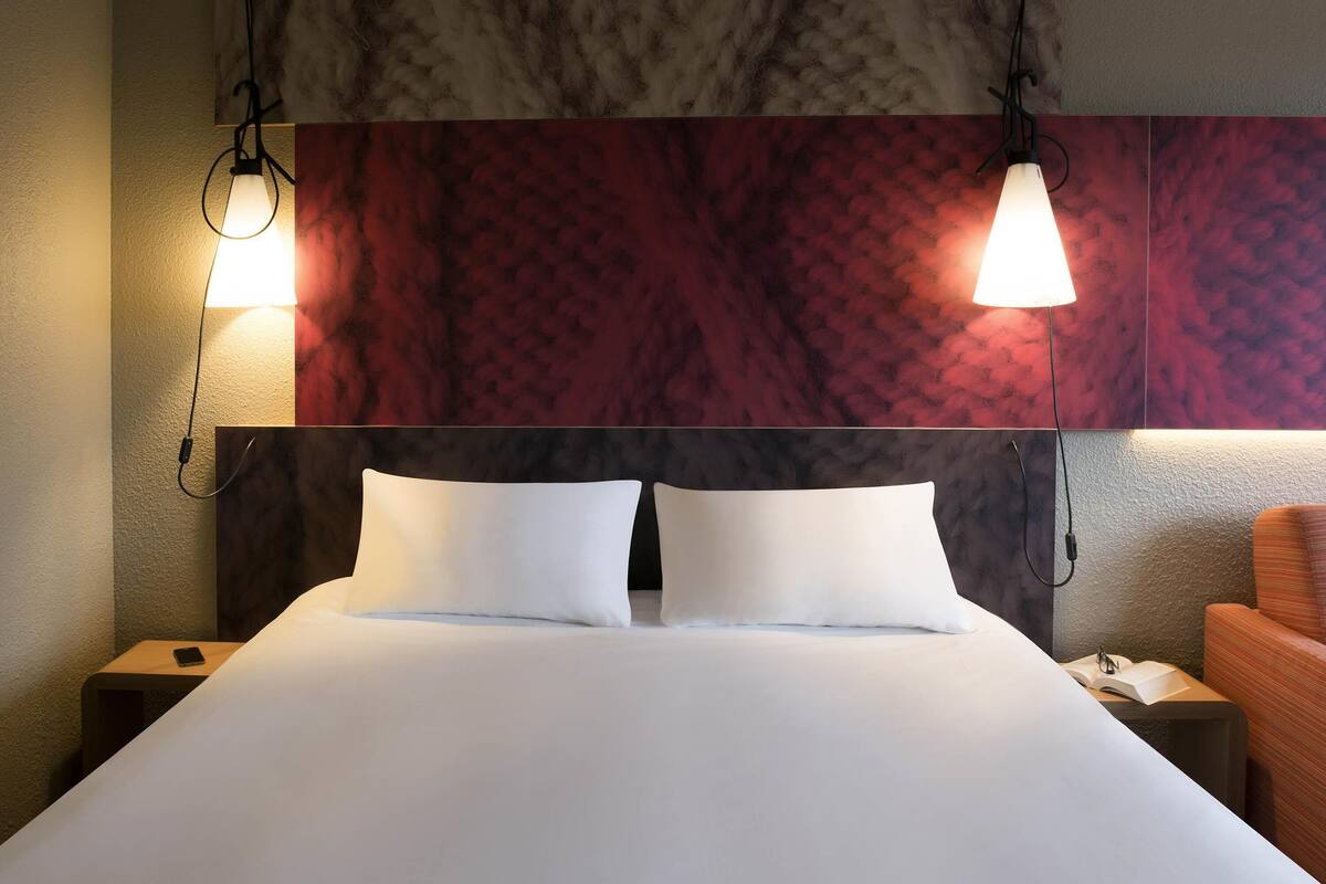 Une chambre d’hôtel avec un grand lit, deux lampes de chevet, une table de chevet avec un téléphone et une chaise.