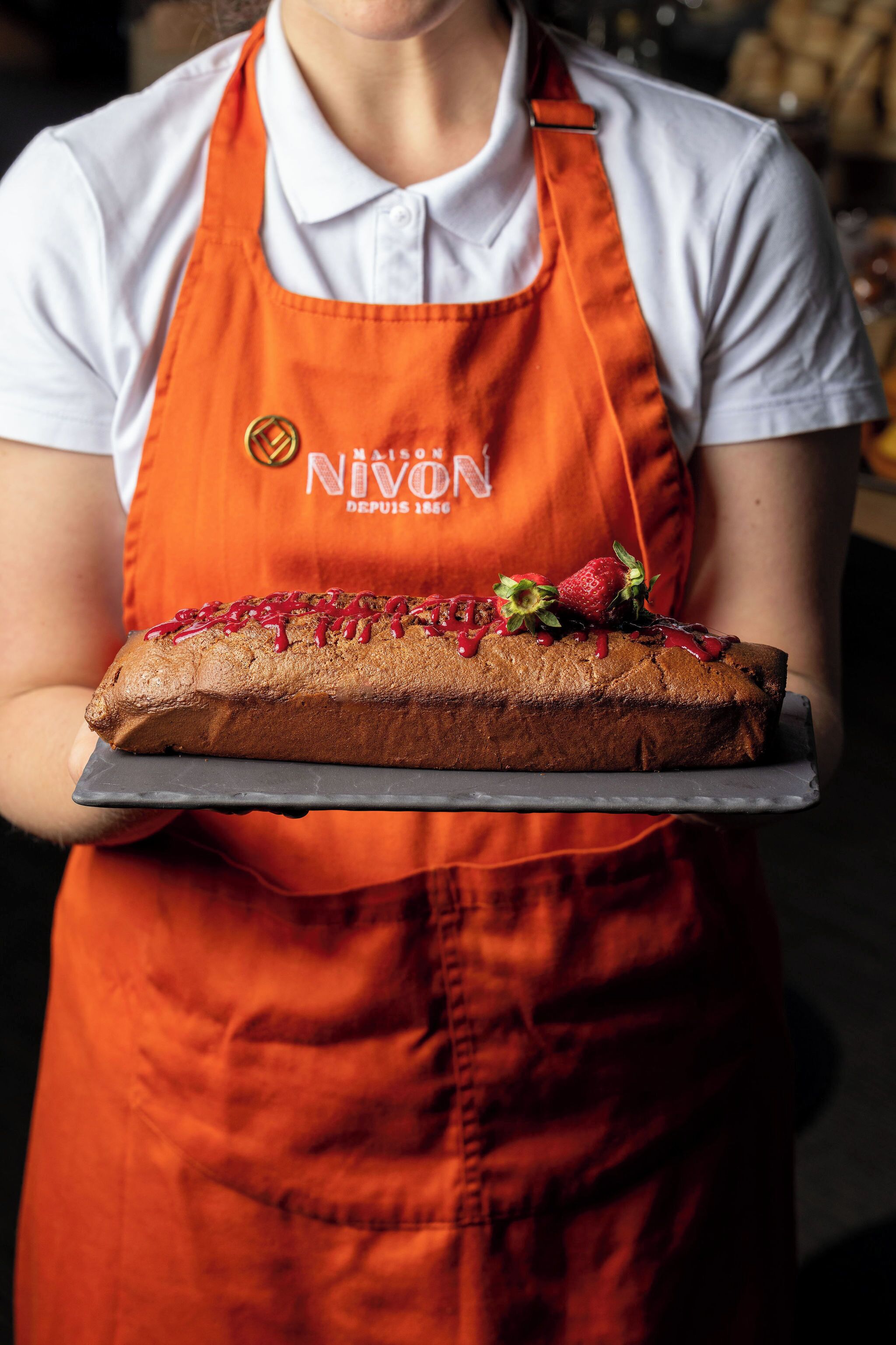 A person holding a loaf of bread with strawberries on top.
