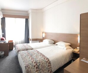 Een hotelkamer met twee bedden, een bureau, een stoel, een telefoon en een raam met gordijnen.