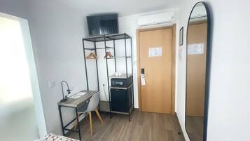 Pieni hotellihuone, jossa on sänky, työpöytä tuolilla, vaatekaappi, peili ja ovi.