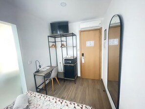 A compact hotel room with a bed, a desk with a chair, a wardrobe, a mirror, and a door. - Flamingo (Lisbon)