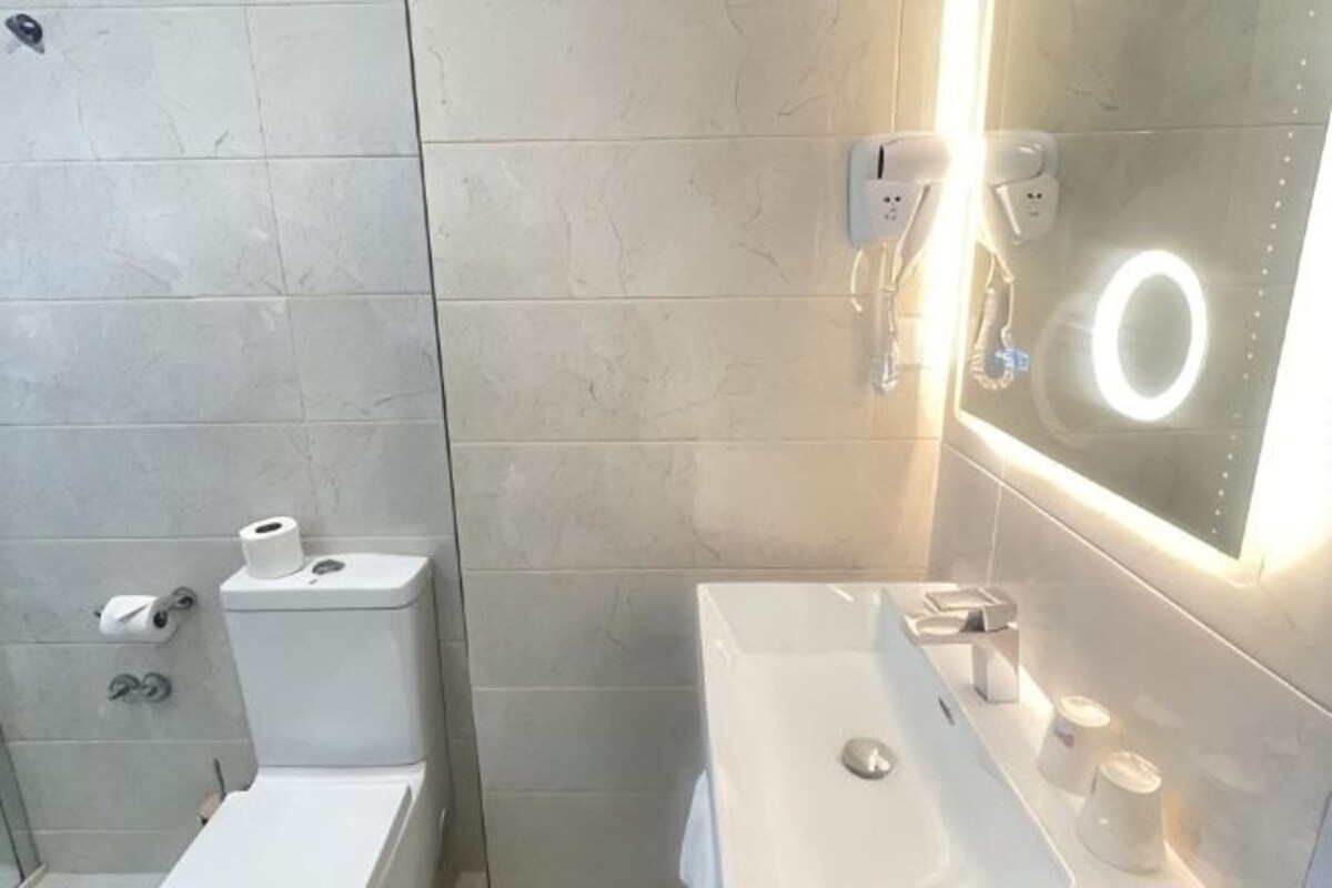 A bathroom with a toilet, sink, and mirror with a lighted ring.