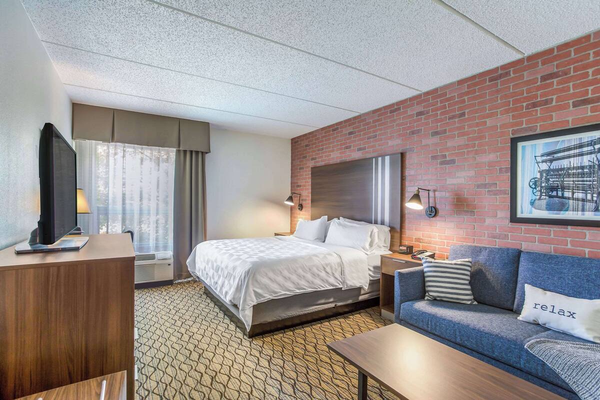 A hotel room with a bed, a sofa, a desk, and a television.