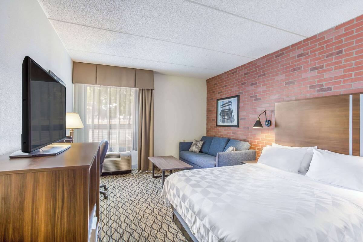 A hotel room with a large bed, a desk with a TV, a couch, and a brick accent wall.