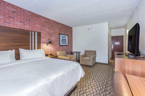 A hotel room with a large bed, two armchairs, a small table, a television, and a brick wall.
