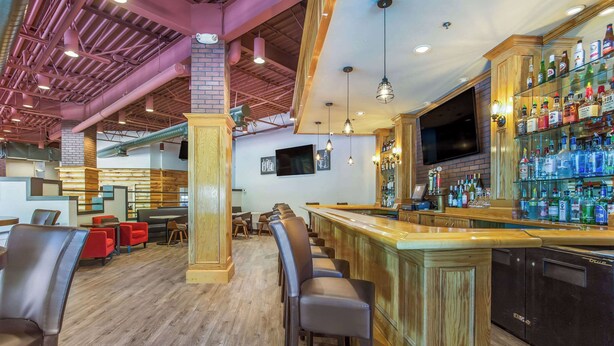 Un espace bar doté d’un long comptoir, de nombreux tabourets et d’une étagère bien garnie de bouteilles d’alcool.