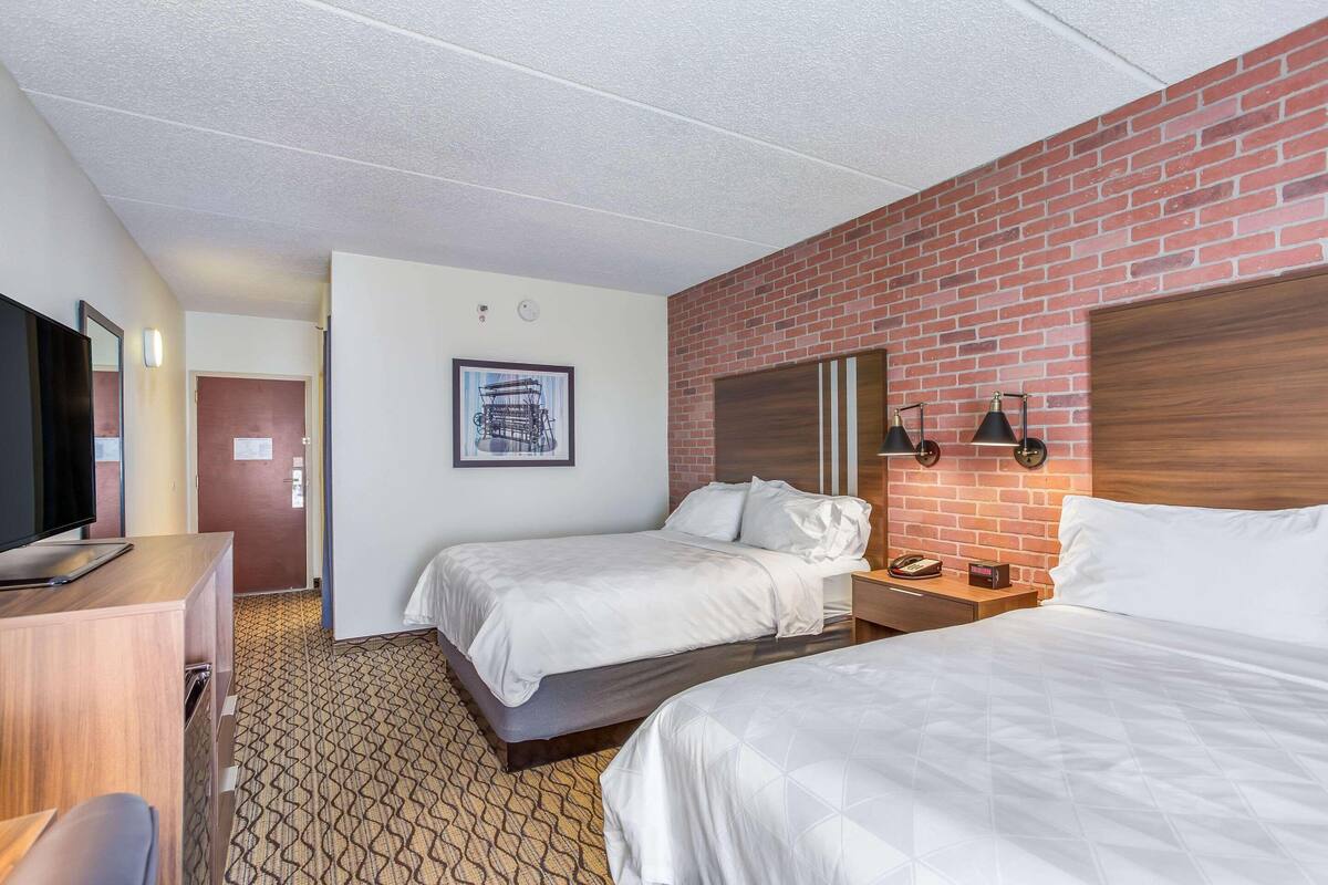 A hotel room with two beds, a desk, a TV, and a brick accent wall.