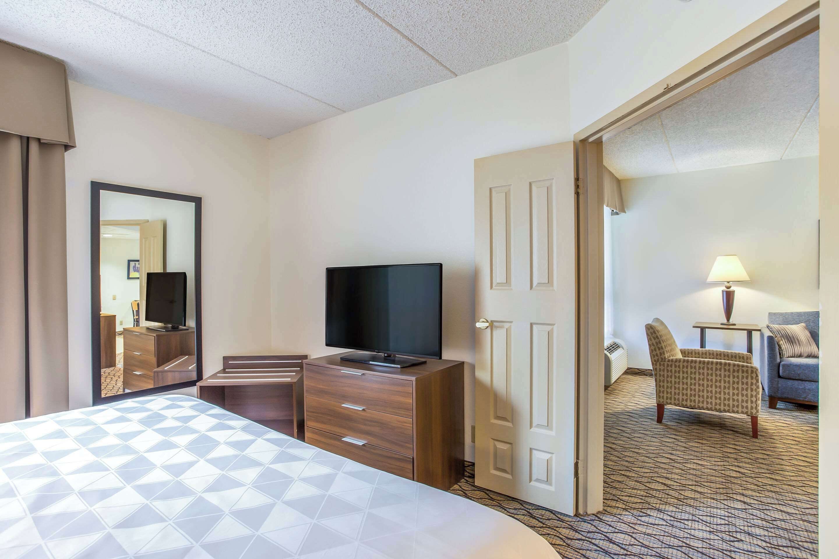 A hotel room with a bed, a TV, a desk, a chair, and a door leading to another room.