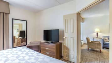 A hotel room with a bed, a TV, a desk, a chair, and a door leading to another room.