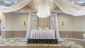 Une salle de banquet où une table est dressée pour un événement officiel, recouverte d’un tissu blanc, et dont le sol est recouvert d’une moquette.