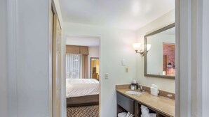 Une salle de bain d’hôtel avec un lit, un lavabo, un miroir et un sol à motifs.
