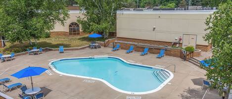 A swimming pool with lounge chairs and umbrellas, surrounded by trees and a building.