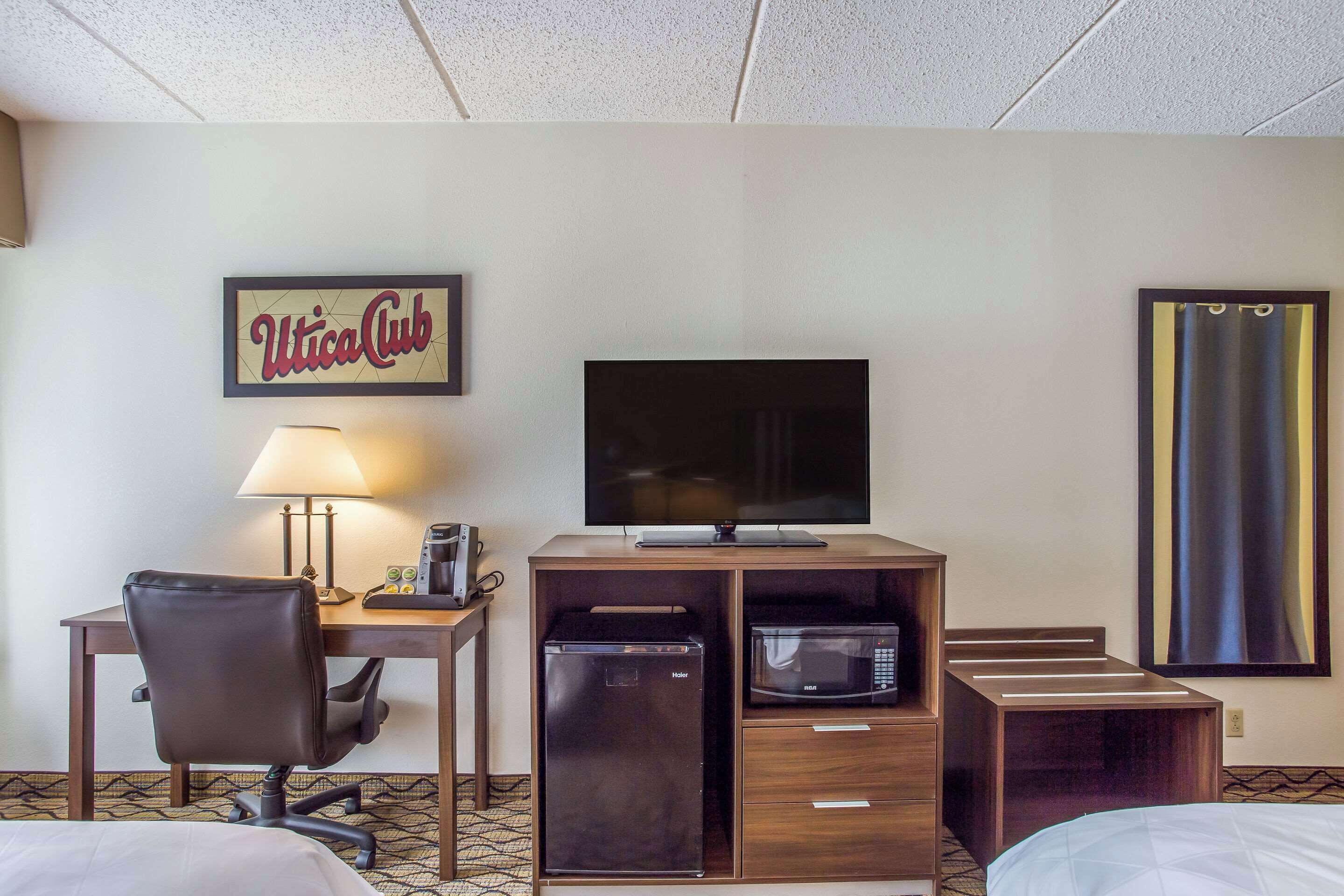 Habitación de hotel con escritorio, silla, televisor, minibar y cama.