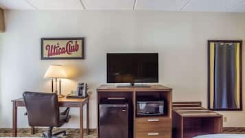 Habitación de hotel con escritorio, silla, televisor, minibar y cama.