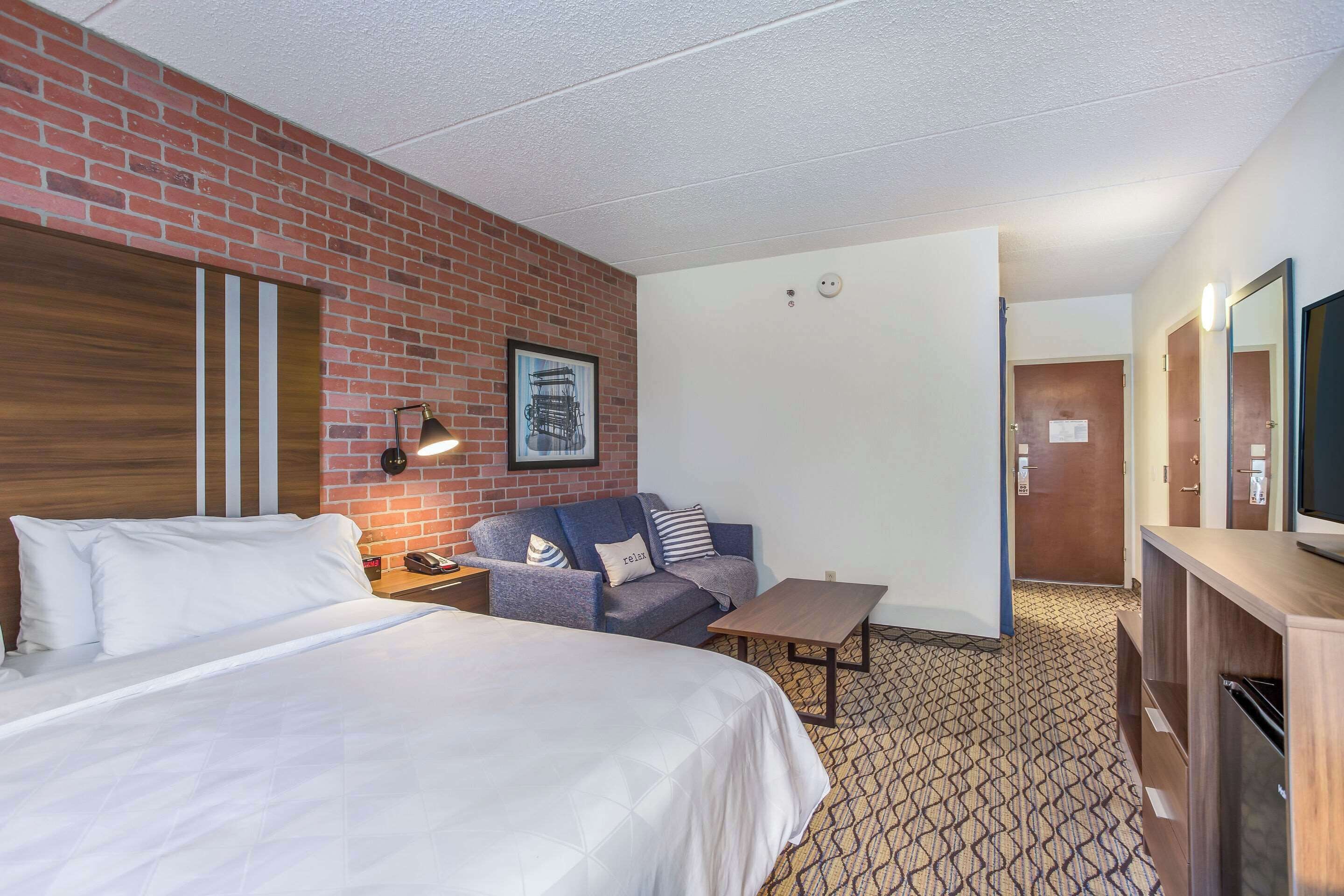 A hotel room with a large bed, a sofa, a small table, and a TV.