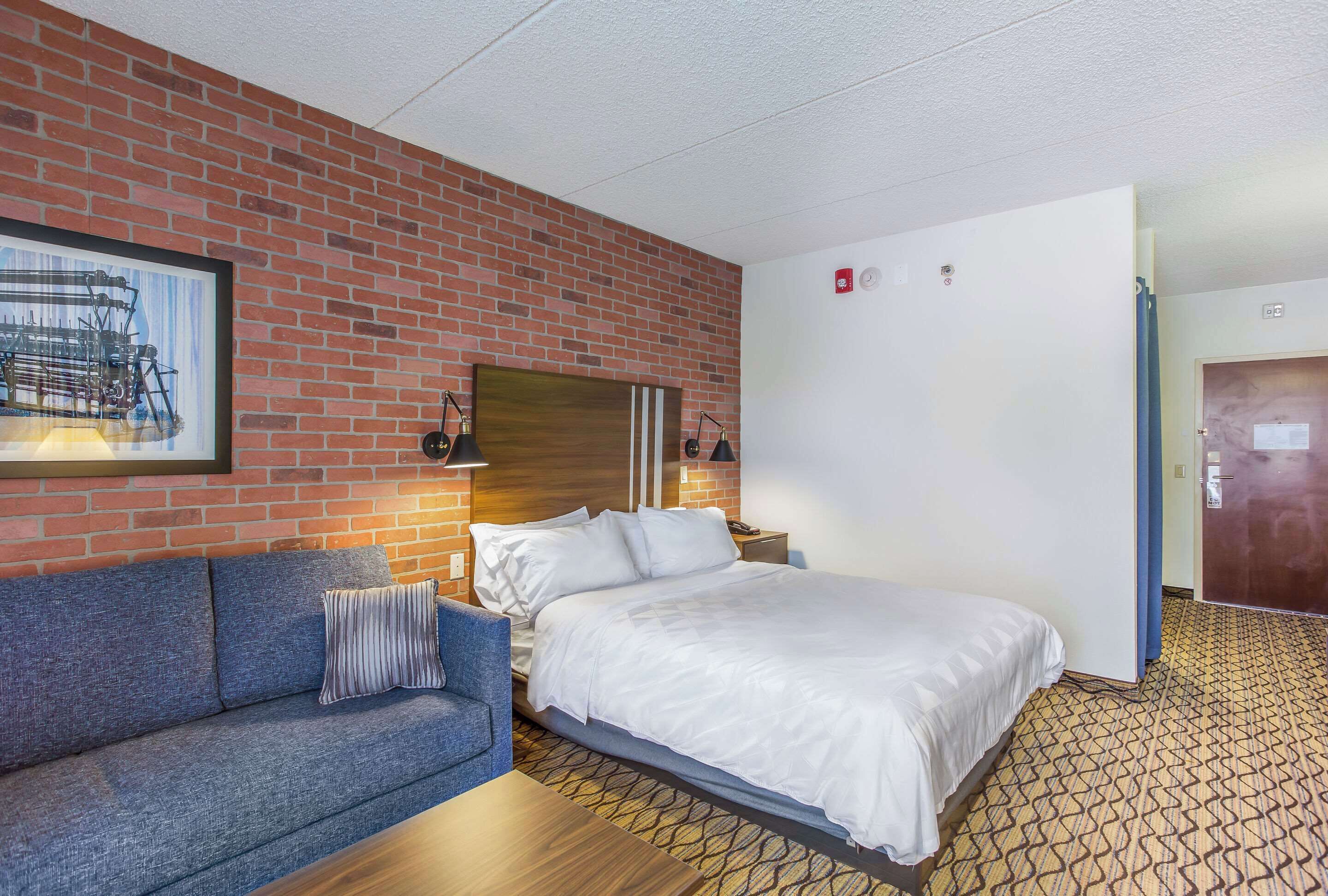 Een hotelkamer met een accentmuur van baksteen, een groot bed, een blauwe sofa en een lijst met een afbeelding erop.