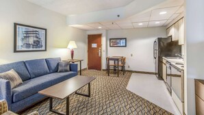 Une chambre d’hôtel compacte comprenant un canapé, une petite table, une kitchenette et une porte donnant accès à la salle de bain.
