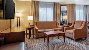 A hotel room with a sofa, armchair, coffee table, and a TV. - Comfort Inn Fairfield Napa Valley Area (Fairfield)