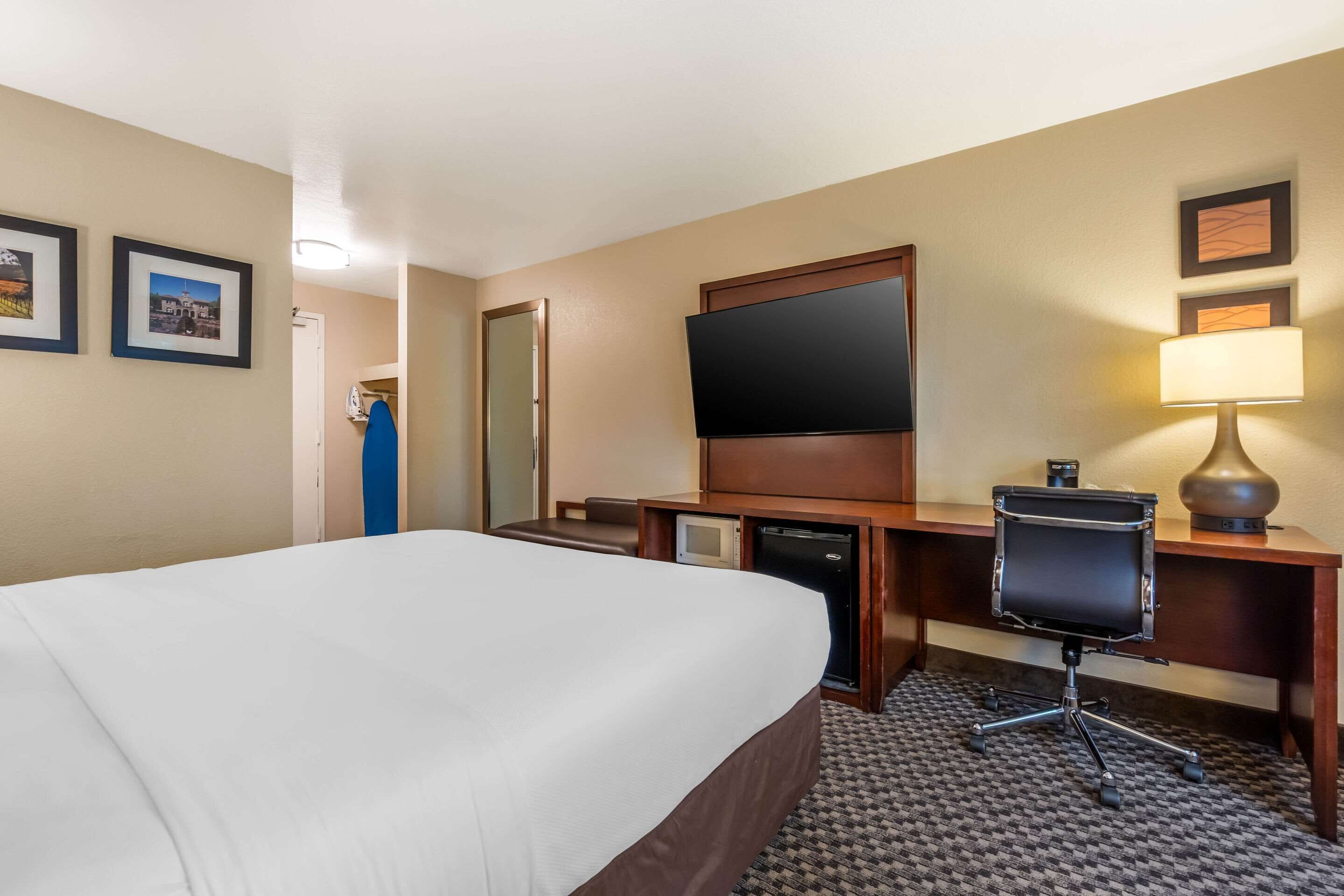 Habitación de hotel con una cama grande, un escritorio con computadora, un televisor y una lámpara.