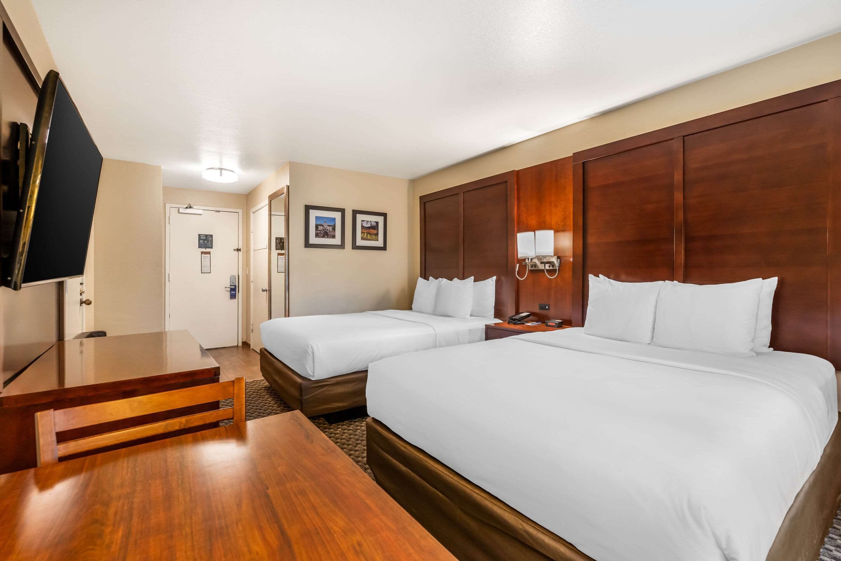 A hotel room with two beds, a wooden desk, a television, and a door leading to a bathroom.
