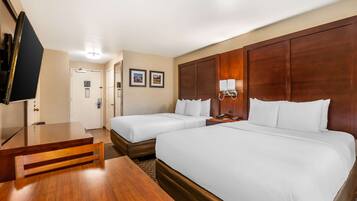 Habitación de hotel con dos camas, un escritorio de madera, un televisor y una puerta que da a un baño.
