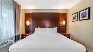A hotel room with a large bed, two bedside tables, a nightstand, a window with curtains, and two wall-mounted lamps.
