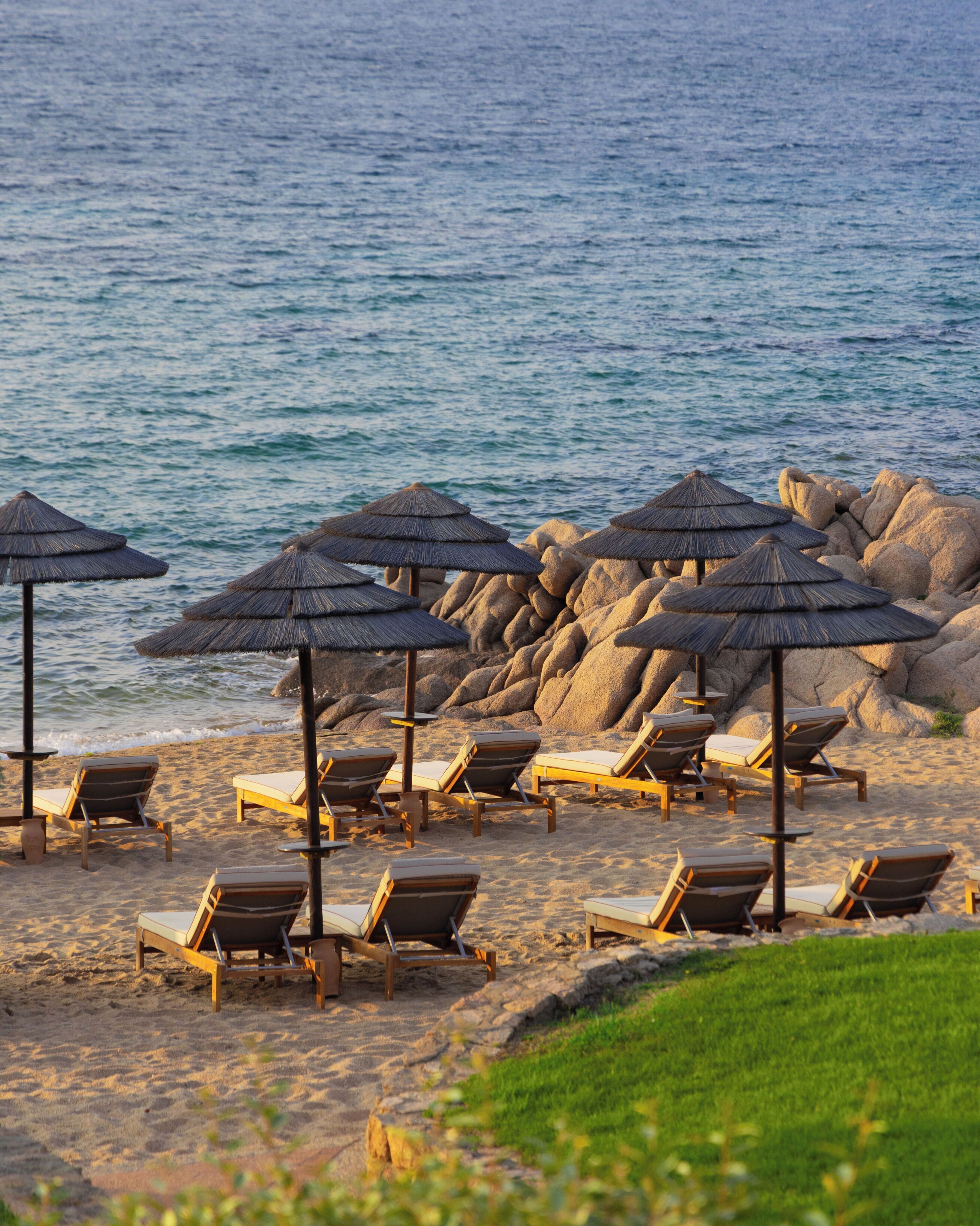 A beach with lounge chairs and thatched umbrellas.
