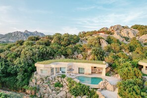 Una villa moderna con piscina, rodeada de paisaje natural y terreno rocoso.