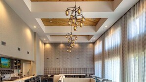 A modern restaurant with wooden flooring, a central seating area with booths, and a bar on the left.