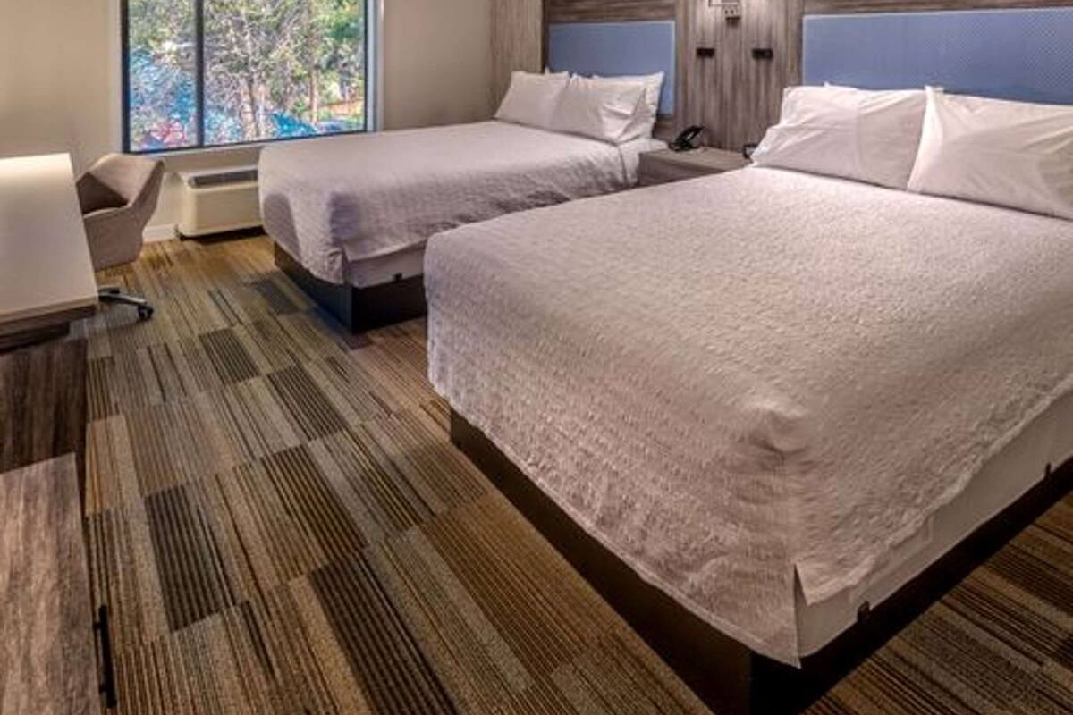 Une chambre d’hôtel avec deux lits, un bureau, une chaise et une grande fenêtre donnant sur des arbres.