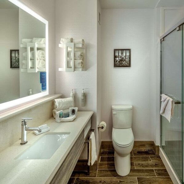 Un baño moderno con un espejo grande, un lavabo, un inodoro y una ducha con mampara de vidrio.