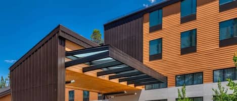 A modern building with a covered entrance, large windows, and a parking area with bicycles.