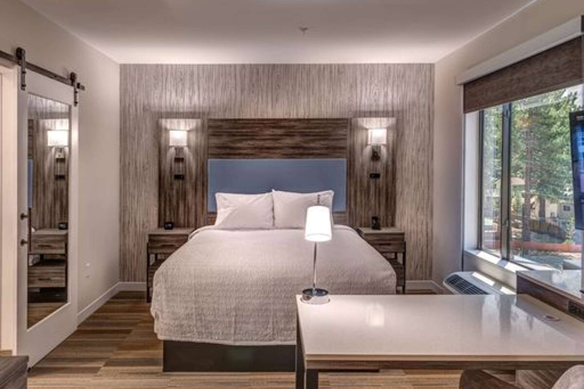 Habitación de hotel moderna con una cama grande, un escritorio y una silla. Una ventana ofrece vistas al exterior.