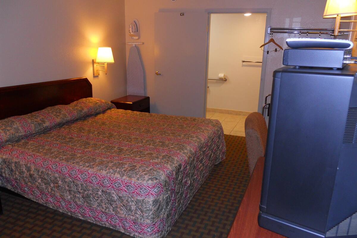A hotel room with a bed, a bedside table, a lamp, a television, and a bathroom door.
