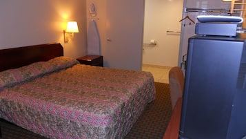 Ein Hotelzimmer mit Bett, Nachttisch, Lampe, Fernseher und einer Badezimmertür.