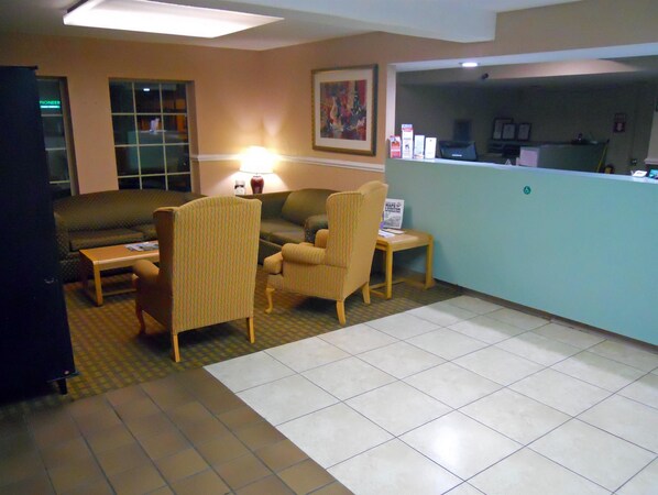 A hotel lobby with a reception desk, a sofa, two armchairs, a coffee table, and a lamp. - America's Best Inn and Suites Beaufort (Beaufort)