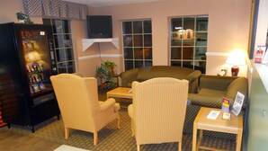 A hotel lobby with a seating area, a vending machine, and a television mounted on the wall. - America's Best Inn and Suites Beaufort (Beaufort)