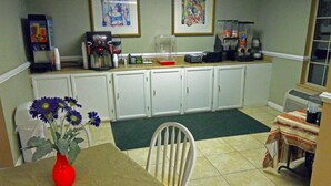 A small kitchen with white cabinets, a coffee maker, and a vase with flowers on the table. - America's Best Inn and Suites Beaufort (Beaufort)
