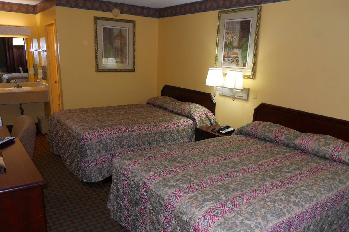 A hotel room with two beds, a desk, a chair, a mirror, and a bathroom.