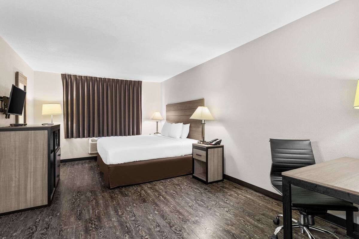 A hotel room with a bed, bedside tables, a desk, a chair, and a television.