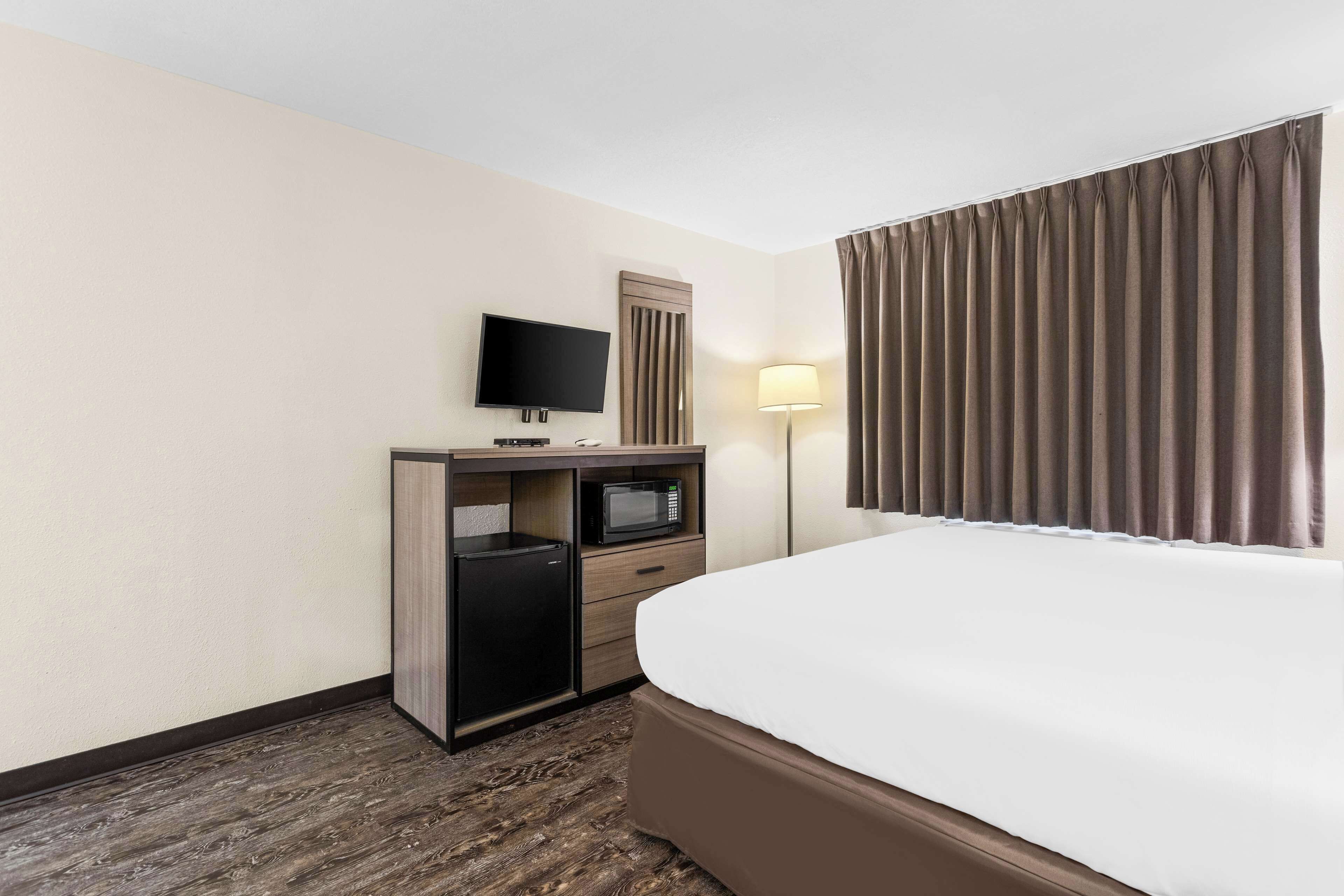 A hotel room with a bed, a desk with a television, a microwave, and a lamp.