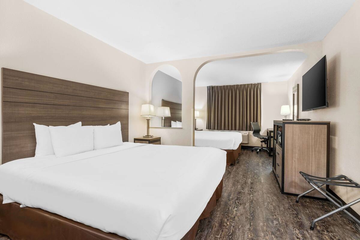 A hotel room with a large bed, a desk, a chair, a television, and a mirror.