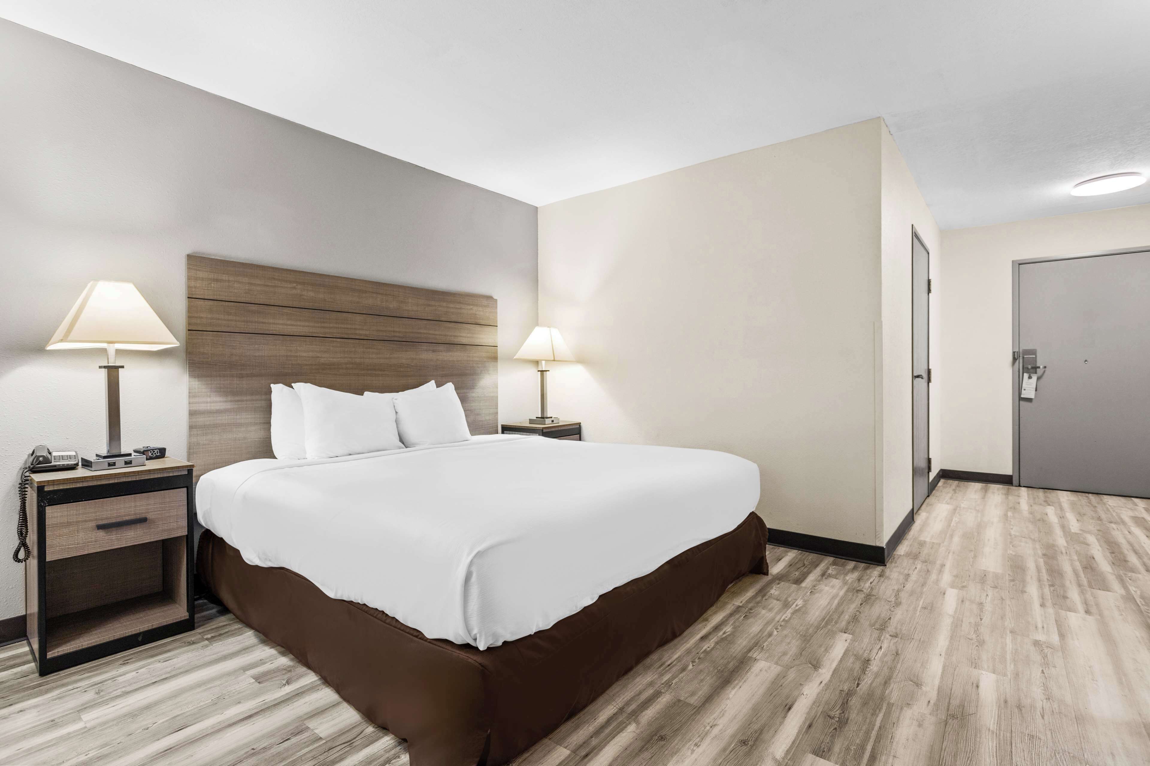 Une chambre d’hôtel avec un grand lit, deux tables de chevet avec des lampes, une tête de lit en bois et une porte.