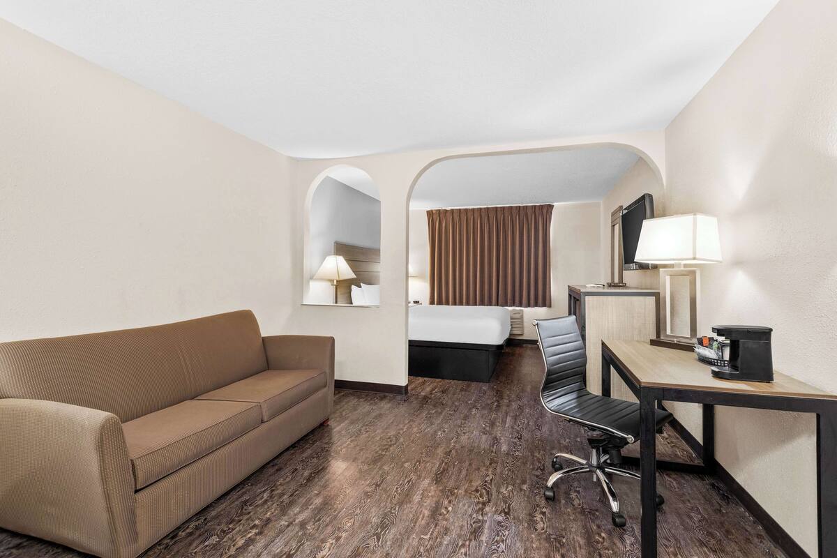 A hotel room with a sofa, a desk with a lamp, a bed with curtains, and a TV.