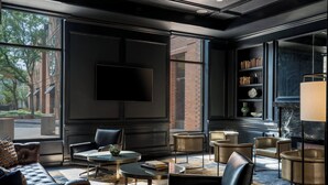 Een moderne lounge met lederen banken, ronde tafels en een flatscreen televisie.