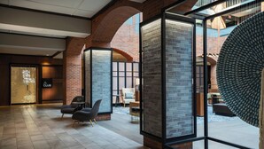 Een ruime lobby met een modern design, met een bakstenen muur, een groot rond raam en een zithoek met stoelen.