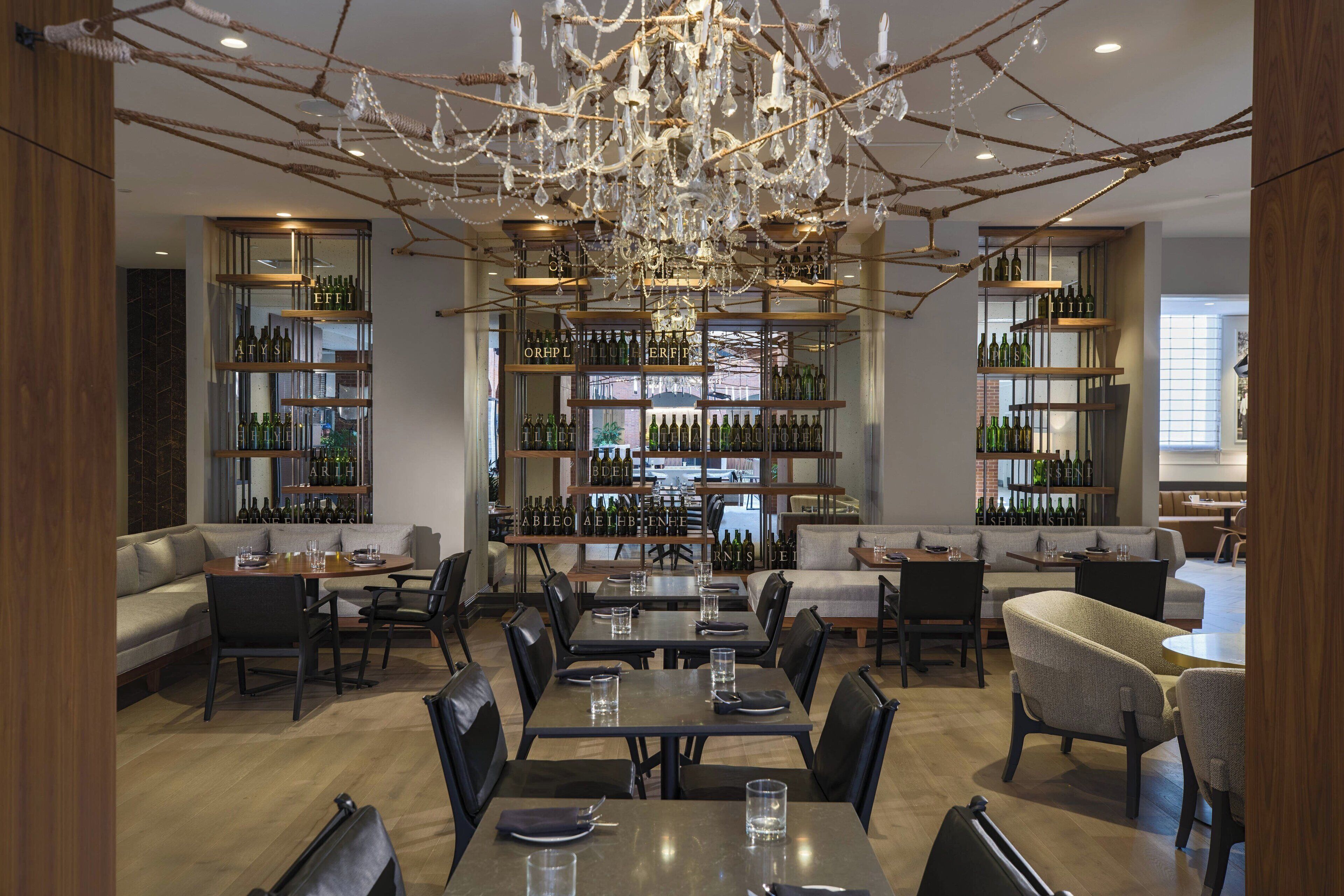 A spacious dining area with multiple tables and chairs, surrounded by shelves of wine bottles.